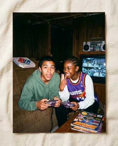 Gaming with [Character] — N64 Era, 1997 1 — Nano Banana AI Prompt: Two friends — a young person with short dark hair and warm brown skin, and a Bla...