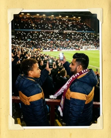 Stadium — Local Derby, Friday Night, 2012 5 — Nano Banana AI Prompt: South Asian guy with neatly gelled black hair and a trimmed beard squeezes in be...