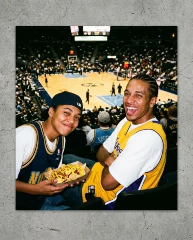 Courtside — NBA Game, 2003 1 — Nano Banana AI Prompt: Two friends — a young person with short dark hair and warm brown skin, hat backw...