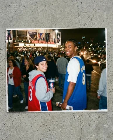 Courtside — NBA Game, 2003 7 — Nano Banana AI Prompt: Flash from the photographer beside them catches their profiles. Film grain, warm...