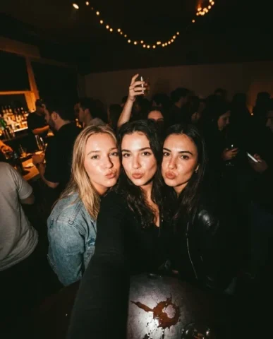 Vintage Flash Indoor Party Group Selfie 6 — Nano Banana AI Prompt: Party selfie with three friends attempting serious expressions but failing to hi...