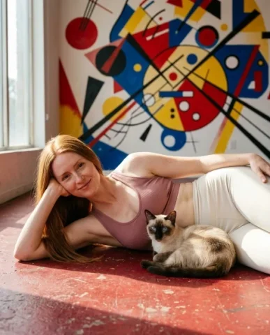 Photorealistic Portrait with Abstract Painted Wall and Cat 1 — Nano Banana AI Prompt: Siamese cat with striking ice-blue eyes and cream-and-chocolate point markings r...