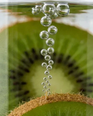 Ultra-Realistic Macro Shot of Fruit in Sparkling Water 5 — Nano Banana AI Prompt: An ultra-realistic photograph capturing the exact moment a fresh kiwi slice drop...