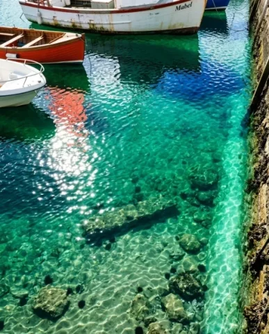 Realistic Coastal Port Scene with Colorful Fishing Boats 4 — Nano Banana AI Prompt: The water is so clear that the harbor floor is partially visible — sandy bottom...