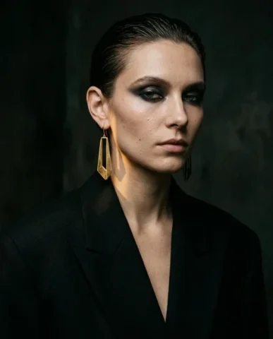 Edgy Smoky Eye Gold Earring Moody Editorial Portrait 1 — Nano Banana AI Prompt: Refined yet daring gold drop earrings with elongated geometric pendant. Moody dr...
