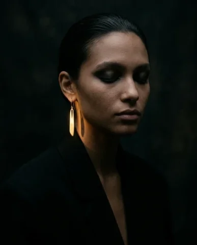 Edgy Smoky Eye Gold Earring Moody Editorial Portrait 6 — Nano Banana AI Prompt: Vertical editorial close-up of a female model in a matte black oversized blazer....