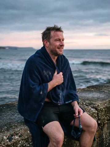 After the Dawn Swim — Nano Banana 2 AI Prompt: A restrained documentary portrait photograph of an original adult male open-wate...