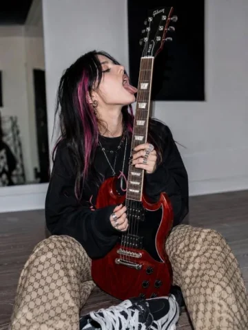 Alternative Rock Guitar Portrait — GPT Image 2.5 AI Prompt: A stylish alternative rock aesthetic photoshoot of a young woman sitting on the...