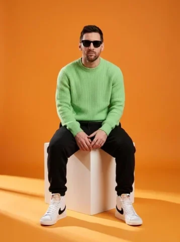 Orange Studio Male Model — Nano Banana 2 AI Prompt: A stylish male model sitting on a white cube in a minimalist studio with a vibra...