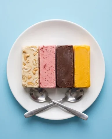 Four-Flavor Kulfi Top Shot — Nano Banana 2 AI Prompt: A quartet of rectangular kulfi slices, featuring distinct flavors of cashew-stud...