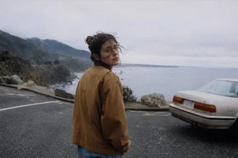 Candid Coastal Portrait — Nano Banana 2 AI Prompt: A cinematic candid photo of a young woman standing in a wet coastal roadside tur...