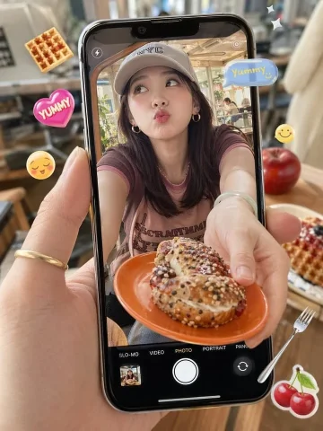 Cafe Food Snapshot — Nano Banana 2 AI Prompt: A photorealistic close-up of a hand holding a modern black smartphone vertically...