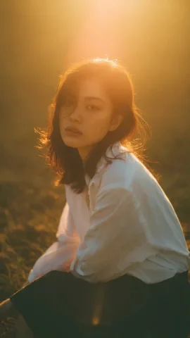 Golden Hour Grassy Field Backlit Halo Dreamy Portrait — Nano Banana 2 AI Prompt: Cinematic portrait of a young woman sitting in a grassy field during golden hour...
