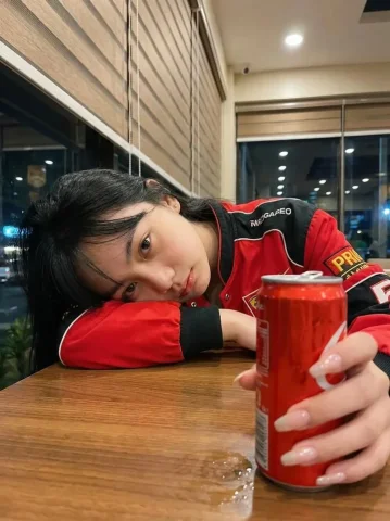 Late Night Cafe Racing Jacket Red Can Portrait — Nano Banana 2 AI Prompt: Ultra-realistic photo of a young woman sitting in a cozy café at night, resting...