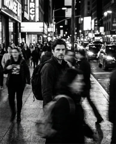 B&W Cinematic Street Portrait with Motion-Blurred Crowd — Nano Banana 2 AI Prompt: A cinematic black and white street portrait of a handsome man standing still in...