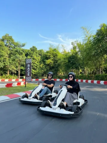 Go-Kart Racetrack Duo Racing — Nano Banana 2 AI Prompt: Two people racing side-by-side in modern white go-karts on a smooth outdoor race...