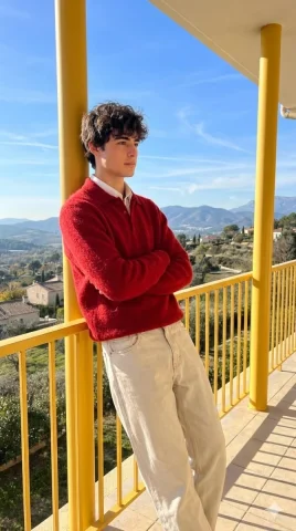 Balcony Red Sweater Boy Mountain View Portrait — Nano Banana 2 AI Prompt: A photorealistic, candid shot of a stylish young man standing on a balcony with...
