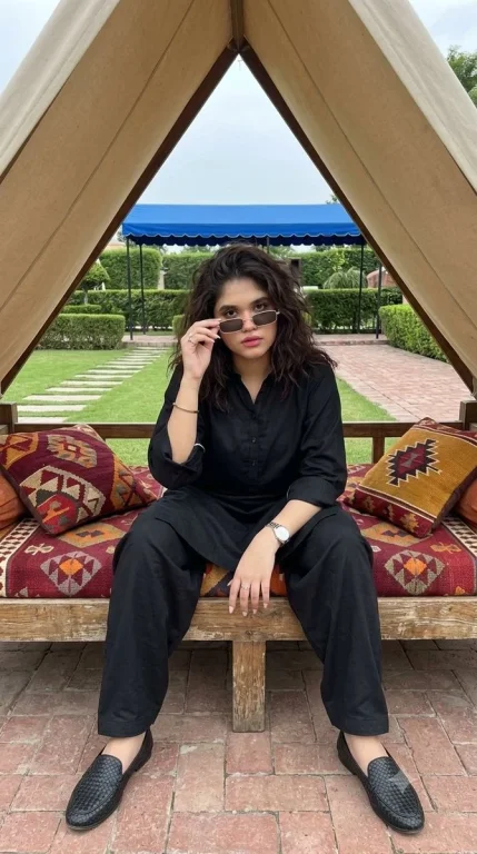 Woman in black kurta seated on daybed under beige canopy
