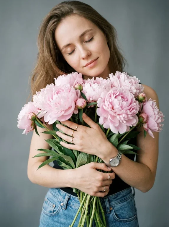 Young woman cradles pale pink peonies in a serene studio portrait