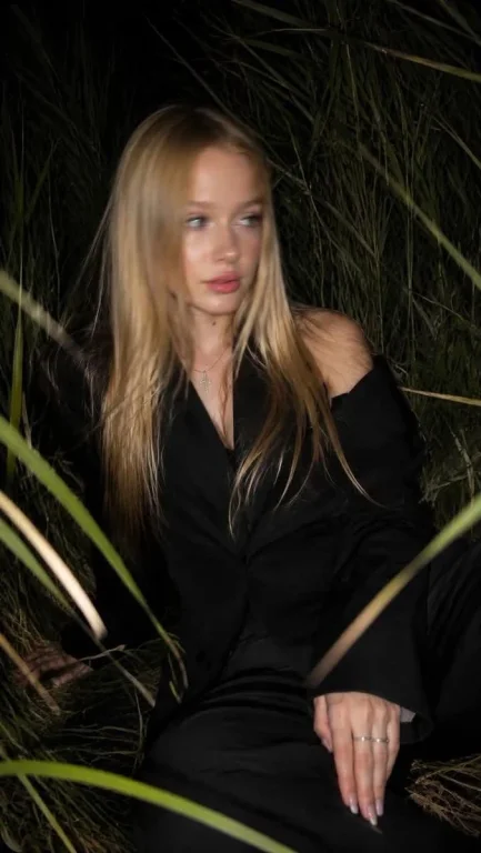 Girl in dark suit sits in tall grass with flash