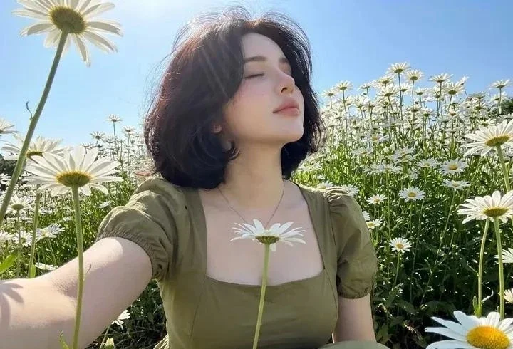 Sunlit daisies frame a porcelain-skinned woman in olive dress