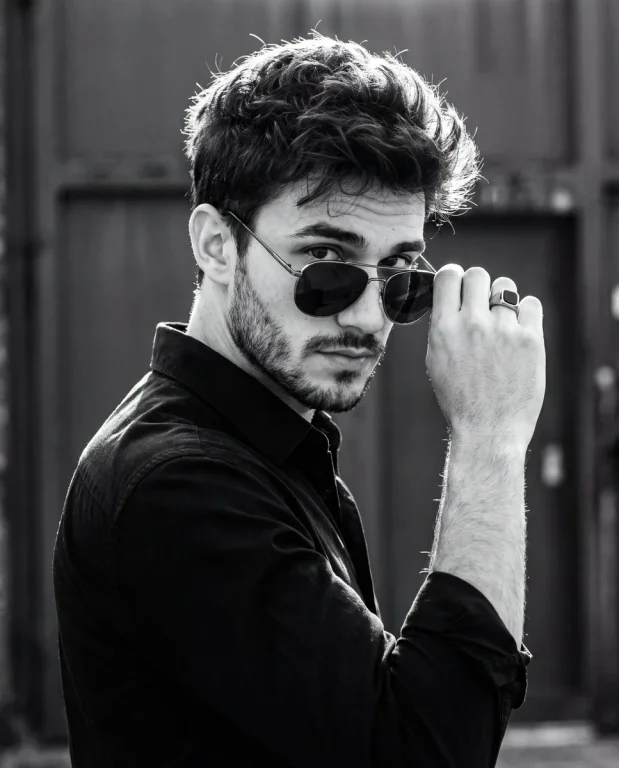 A confident man grips his aviator sunglasses in dramatic monochrome