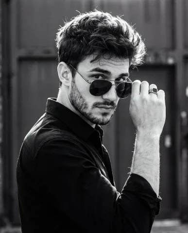 A confident man grips his aviator sunglasses in dramatic monochrome — Nano Banana 2 AI Prompt: A cinematic high-contrast black-and-white portrait captured in a 4:5 vertical co...