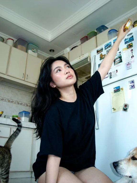 A woman stretches to grab an item on top of the refrigerator