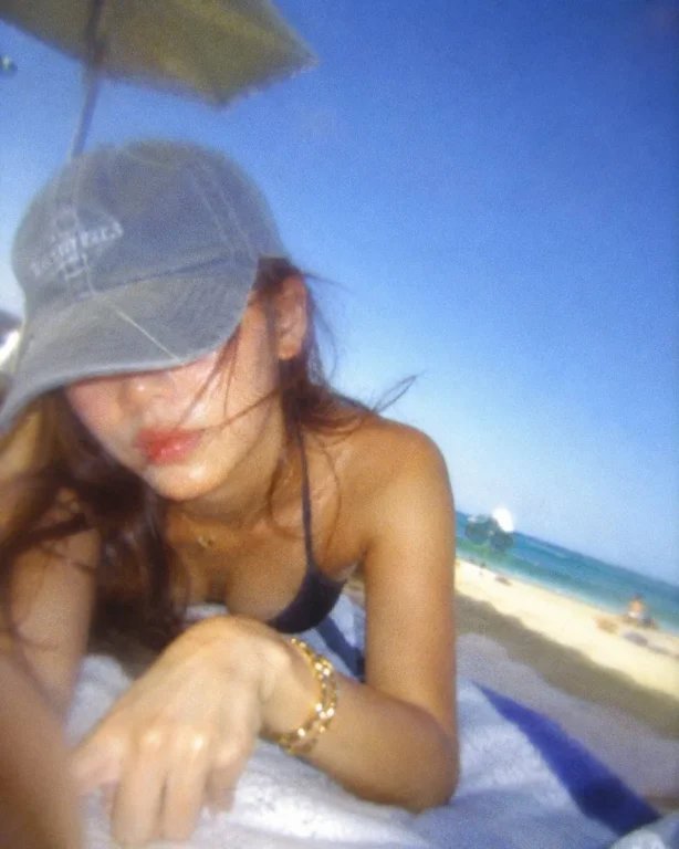 A woman in a baseball cap traces patterns on a towel by the sea