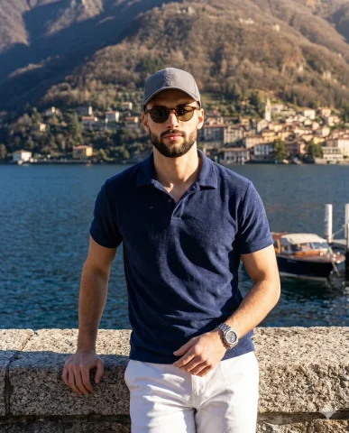 Man in navy polo leans on granite wall by Lake Como — Nano Banana 2 AI Prompt: A handsome, fit man is positioned in a center composition, leaning confidently a...