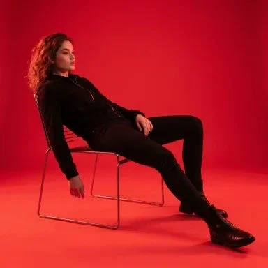 A confident woman in black reclines on a metal chair