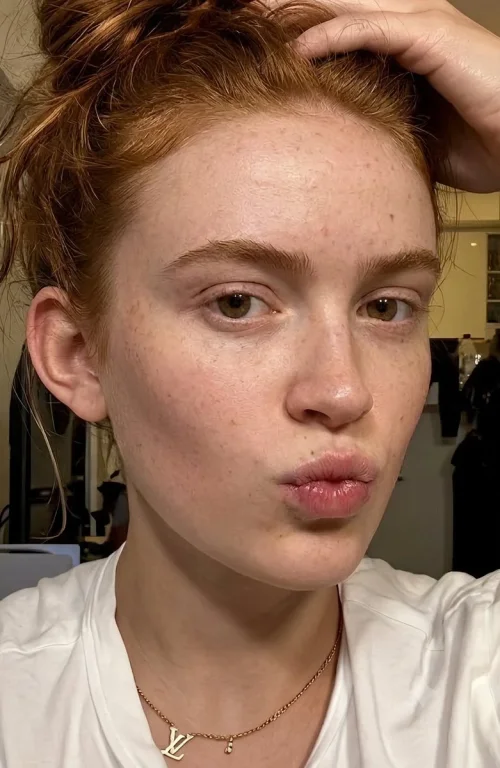 Auburn-haired woman with freckles puckers lips in natural light