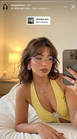 A woman with rhinestone glasses takes a golden selfie on white bedding — Nano Banana 2 AI Prompt: Ultra-photorealistic vertical 9:16 Instagram Story-style selfie of a beautiful y...