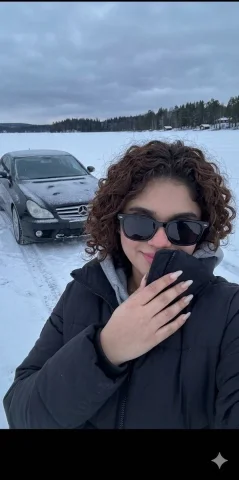 Chill Vibes: A Stylish Snapshot on Frozen Terrain — Nano Banana 2 AI Prompt: A young woman wearing a black winter puffer jacket and a gray hoodie is taking a...