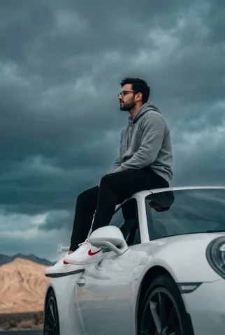 Stormbound Elegance on a Porsche Roof — Nano Banana 2 AI Prompt: A low-angle, medium-shot photograph of a young man with glasses and a groomed be...