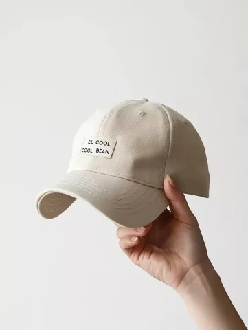 Beige Baseball Cap Photography — Midjourney v6 AI Prompt: Product photograph of a beige baseball cap with embroidered text "EL COOL BEAN",...