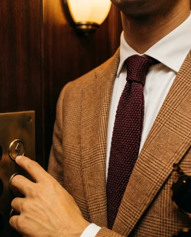 Vintage Elevator Warm Glen-Plaid Suit 5 — Nano Banana AI Prompt: Detail shot inside a vintage Art Deco elevator. Tight framing on the upper chest...