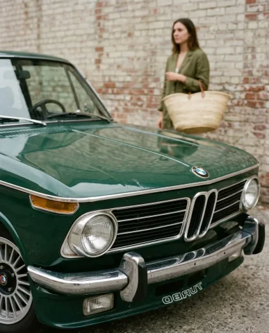 Vintage BMW Street Style with Straw Tote 7 — Nano Banana AI Prompt: Close-up detail shot of the front end of a Forest Green 1974 BMW 2002 Turbo. Sha...