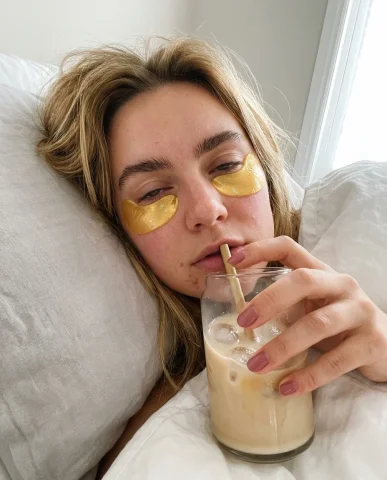 Morning Skincare Selfie with Under-Eye Patches 1 — Nano Banana AI Prompt: Overhead flat lay on rumpled pale gray linen sheets. Center: an open packet of g...