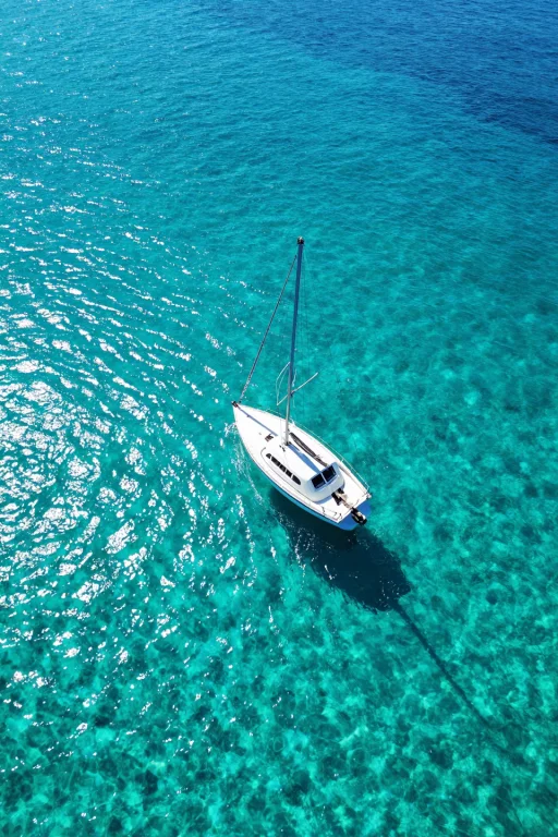 Aerial Top-down View Of A Single White Sailboat With Its Mas...