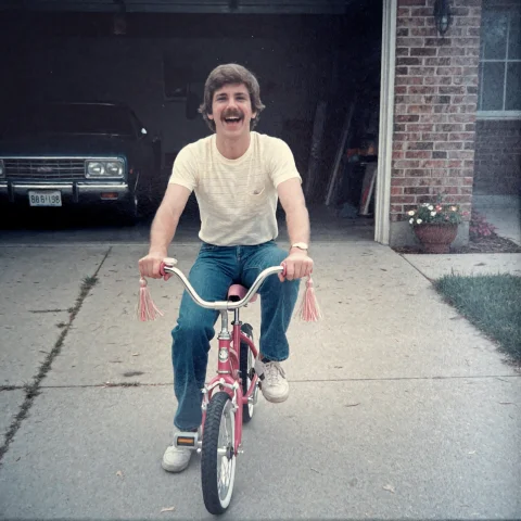 Young Man On Child's Bike Prompt — Stable Diffusion AI Prompt: faded80s, a young man with a scraggly moustache is riding a bicycle in the drive...