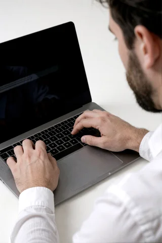 Over-the-shoulder Close-up Of A Man With A Dark Beard Typing... — Stable Diffusion AI Prompt: Over-the-shoulder close-up of a man with a dark beard typing on a silver laptop....