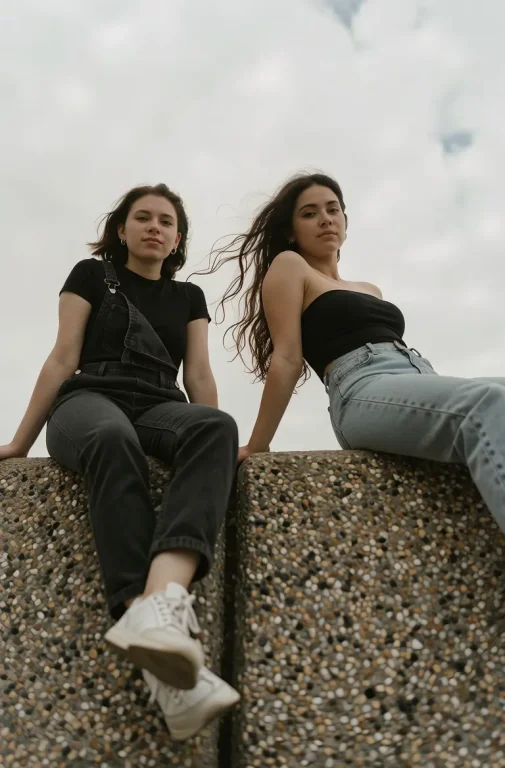 Low Angle Shot Of Two Young Women Sitting On A Textured Conc...