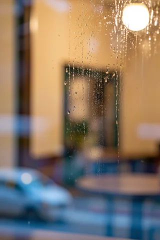 A Rain-streaked Window Merging Warm Interior And Cold Street... — Stable Diffusion AI Prompt: A rain-streaked window merging warm interior and cold street into one layered im...