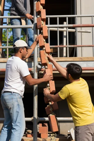 Builders Passing Bricks Hand-to-hand Up A Scaffold Chain, Mi... — Stable Diffusion AI Prompt: Builders passing bricks hand-to-hand up a scaffold chain, mid-transfer grip, mor...