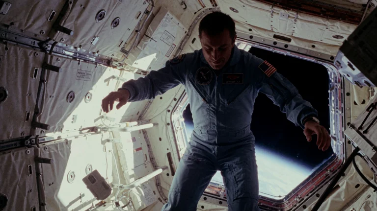 A Cosmonaut In A Blue Flight Suit Floats Weightlessly Throug...