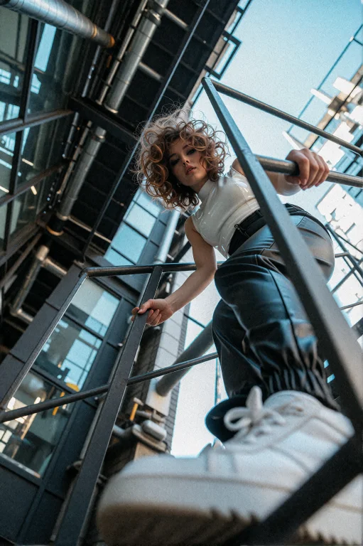 A Woman With Short Voluminous Curly Brown Hair Climbs An Out...