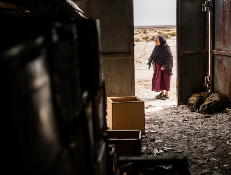 An Elderly Woman In A Dark Woven Shawl And Long Maroon Dress...