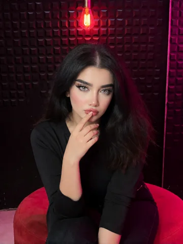 A Young Woman With Long, Wavy Black Hair And Pale Skin, Sitt... — Stable Diffusion AI Prompt: a young woman with long, wavy black hair and pale skin, sitting on a red circula...